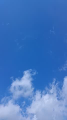 Time-lapse video of fast-moving fluffy white clouds rushing across the bright blue sky on a windy day.