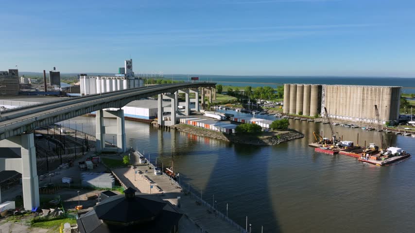 Aerial view of the Buffalo Skyway over the Buffalo River, featuring industrial grain silos, construction barges, and the waterfront in Buffalo, New York, United States.