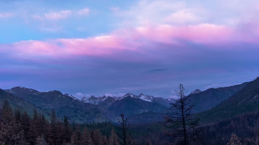 Mountains landscape timelapse in Stanley Idaho with colorful twilight clouds shifting over snow capped peaks and evergreen forests at dusk
