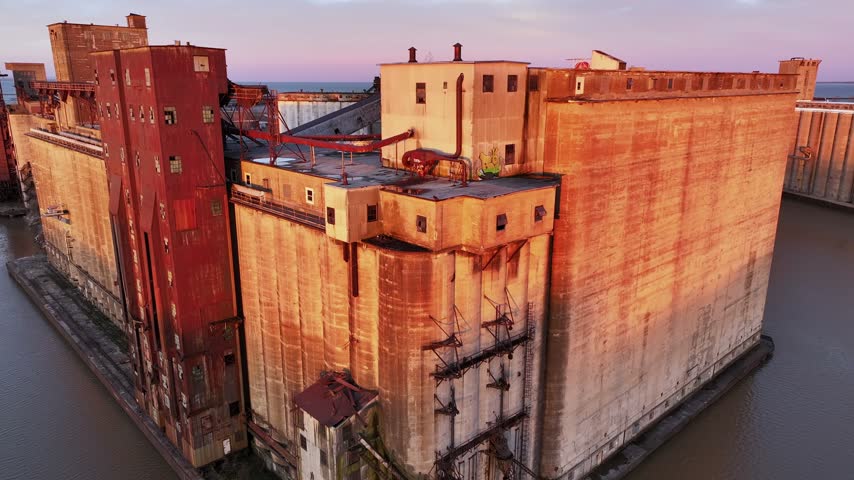 Aerial view of abandoned grain silos and the S.S. Columbia moored in the Buffalo River bathed in warm morning sunlight in Buffalo, New York, United States.