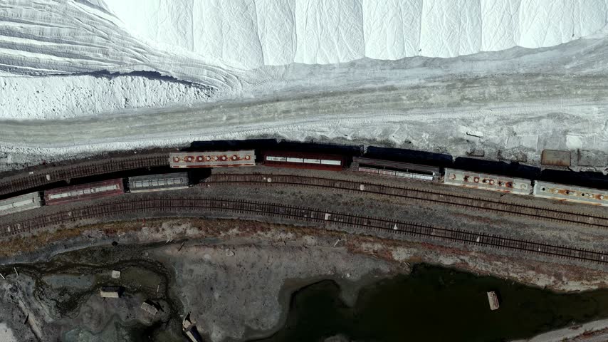 Aerial view of freight train tracks running alongside massive white mounds of harvested sodium chloride salt near the Great Salt Lake in Ogden, Utah, United States.