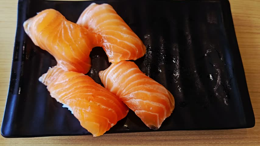 Four pieces of raw fish sushi, arranged on a plate and ready to be served.
