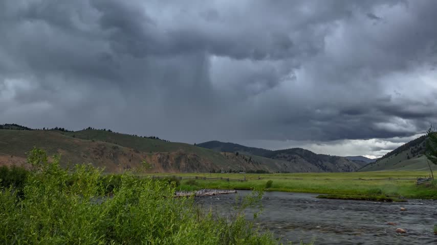 Stanley Idaho mountain valley timelapse showing dark storm clouds moving rapidly across the sky above a winding river and grassy meadows