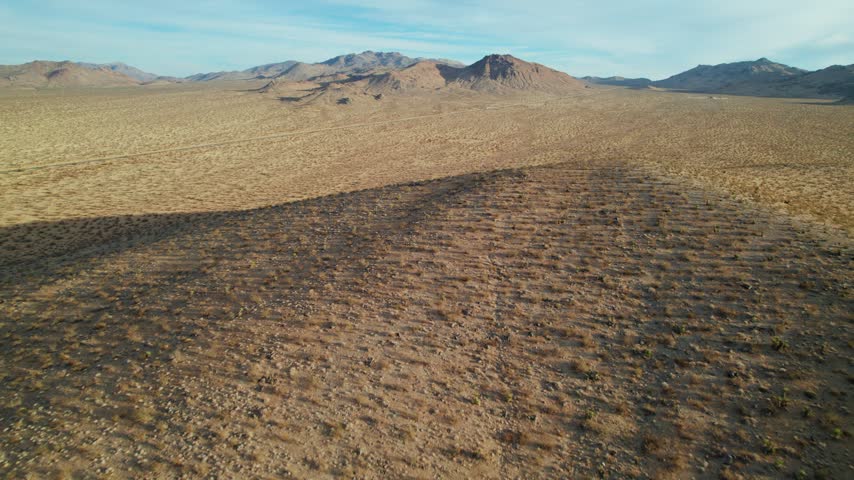Drone flying low over desert plains toward volcanic hills in the Mojave