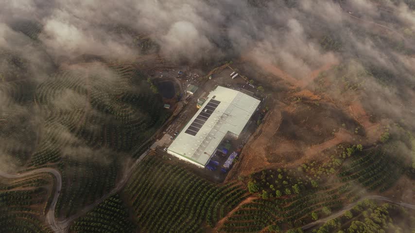Aerial view of industrial facility with solar panels on the roof surrounded by agricultural fields and mist in El Campillo, Andalusia, Spain.