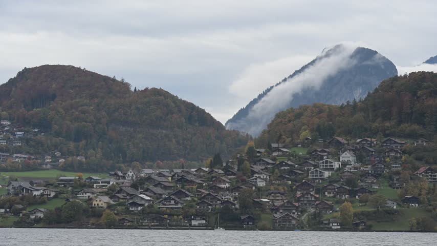 Swiss lakeside town lies beneath cloud covered mountains, representing alpine travel, waterfront landscape, European tourism, dramatic weather, peaceful scenery, and Bernese Oberland environment.