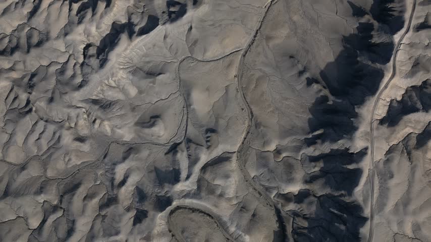 Aerial view of the rugged desert landscape near Hanksville, featuring intricate eroded rock formations, dry terrain, and winding dirt paths in Hanksville, Utah, United States.