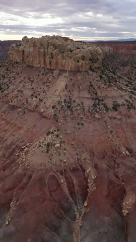 Aerial view of a rugged desert butte with red rock formations and eroded slopes under a cloudy sky in Utah, United States.