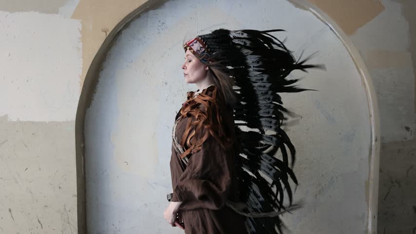 Profile of a woman in long black and white feather headdress against an arched wall. Clean composition with copy space for text and layout.