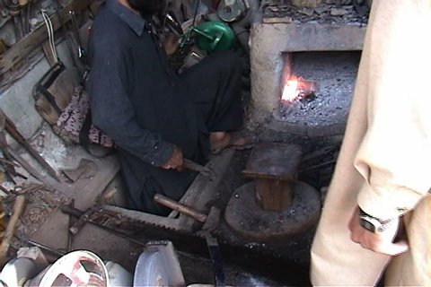 WANA, SOUTH WAZIRISTAN, PAKISTAN - AUGUST 01, 2002: Blacksmith removes axe blade from oven and sharpens it with a metal file.