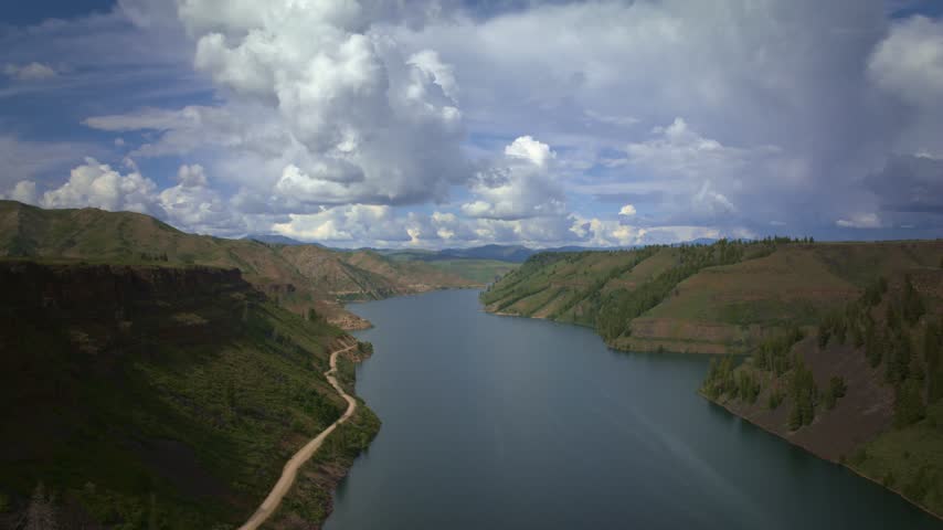 USA reservoir timelapse capturing fast moving clouds above a deep canyon lake surrounded by forested hills and an isolated dirt road