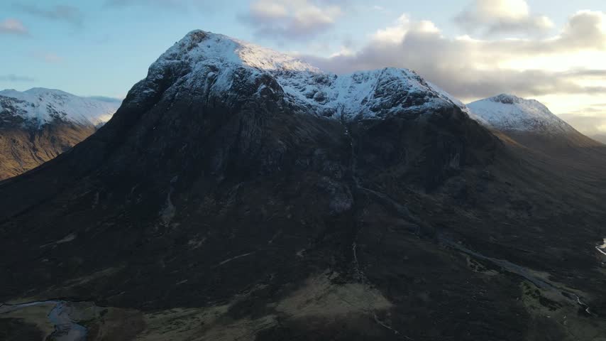 Aerial view of the snow-capped peaks of Glencoe, featuring rugged mountain slopes and dramatic lighting in Glencoe, Scotland, United Kingdom.