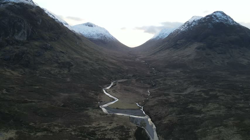 Aerial view of the winding river through the snow-capped mountains of Glencoe, Scotland, United Kingdom.
