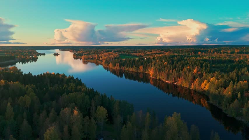 Aerial drone view of serene Finnish lake surrounded by colorful autumn forest at sunset