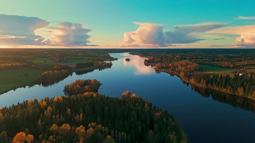 Aerial drone view of serene Finnish lake surrounded by colorful autumn forest at sunset