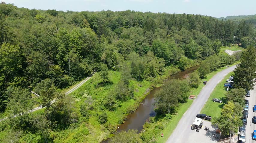 Slow aerial drone flight above a dark river winding beside a road and green summer forest near the mountain town of Thomas, West Virginia, USA.