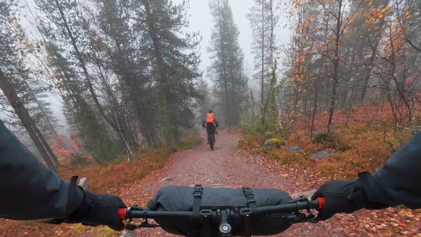 Father and son mountain bike riding on misty trail during autumn ruska season in Finland