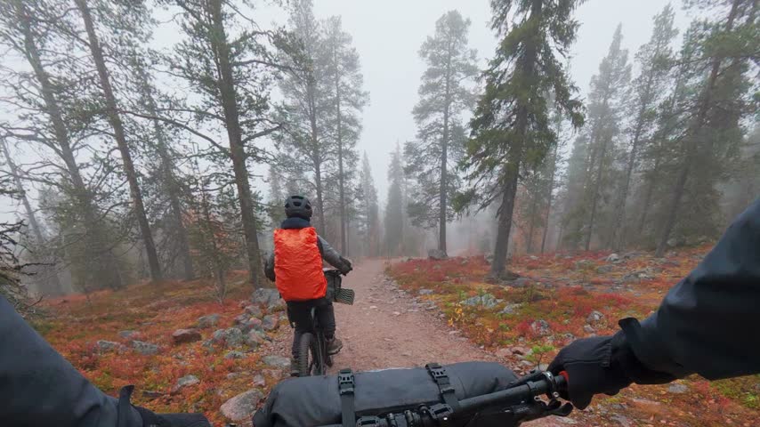 Father and son mountain bike riding on misty trail during autumn ruska season in Finland