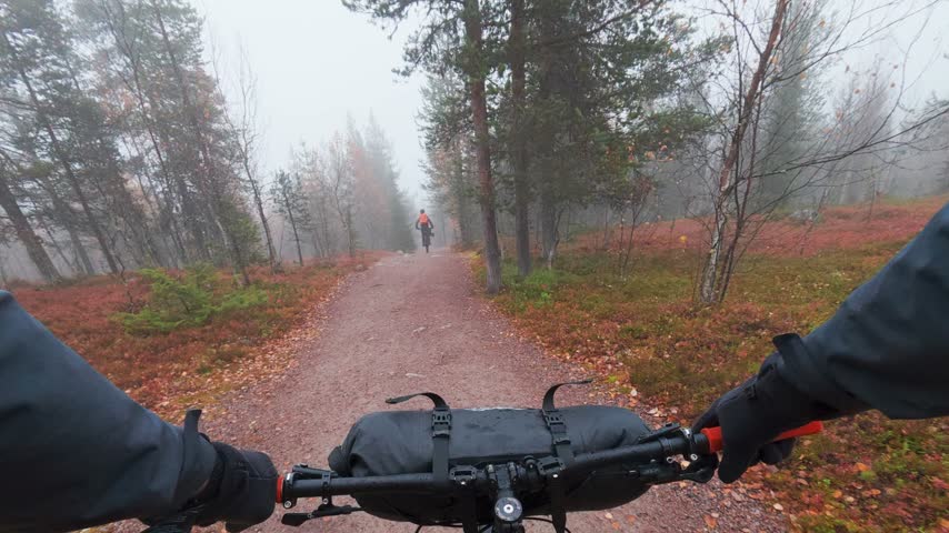 Father and son mountain bike riding on misty trail during autumn ruska season in Finland