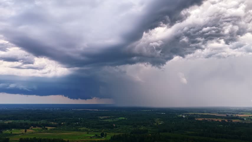 Aerial view of dark storm clouds and heavy rain over the green fields and forests near Ventspils, Latvia.