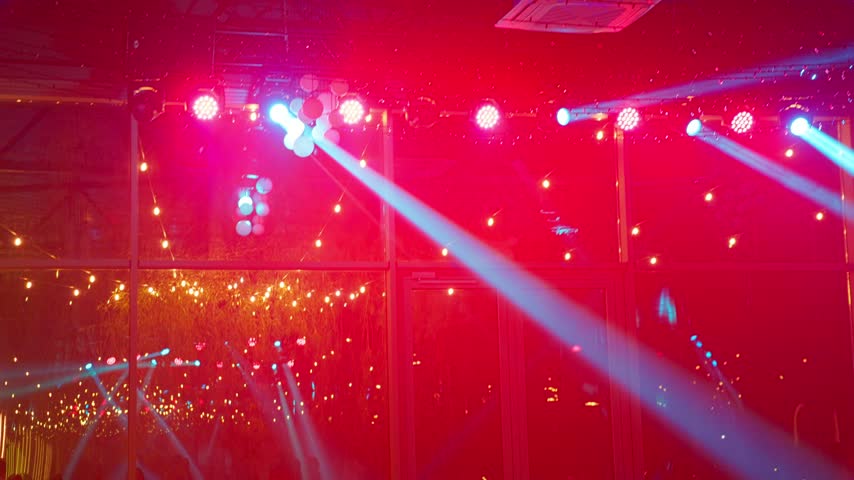 Bright green stage spotlights and cyan laser beams sweep across the dark ceiling and panoramic glass walls decorated with warm festive string lights inside a lively night party venue.