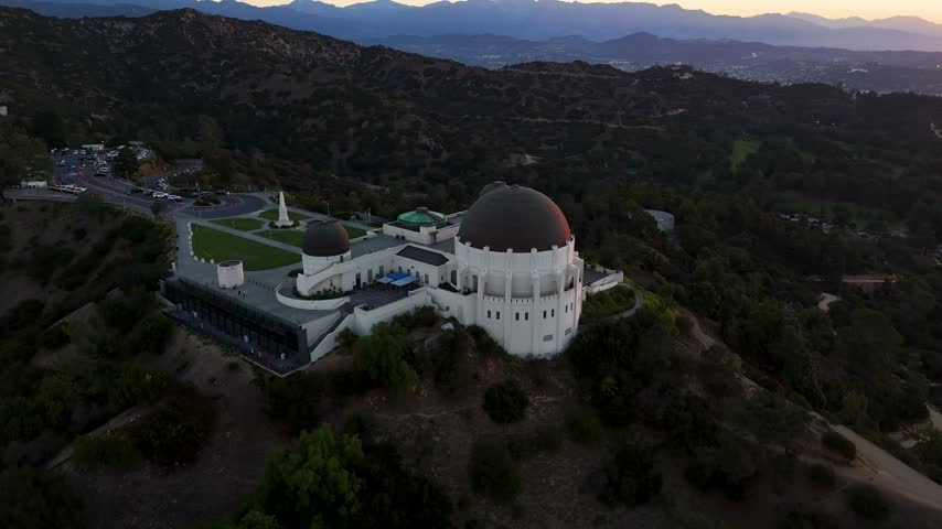Aerial view of the iconic Griffith Observatory perched on Mount Hollywood, featuring its distinctive domes and surrounding parkland in Los Angeles, California, United States.