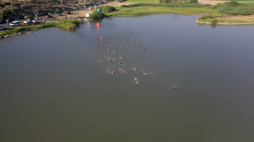 Aerial view of swimmers participating in a triathlon in a lake with a shoreline and parked cars visible in Cody, Wyoming, United States.