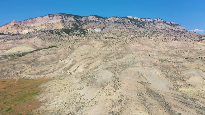 Aerial view of arid mountain landscape with rocky slopes and sparse vegetation under a clear blue sky in Cody, Wyoming, United States.