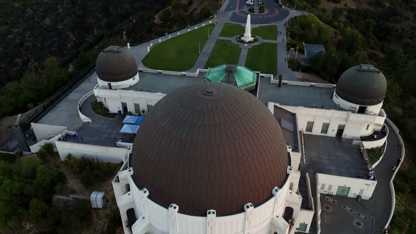 Aerial view of the iconic Griffith Observatory with its distinctive domes and surrounding park grounds in Los Angeles, California, United States.