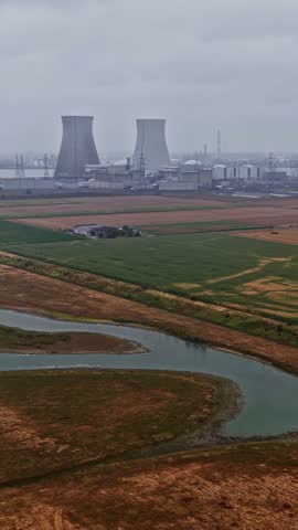 Aerial view of the Doel Nuclear Power Station with its iconic cooling towers and industrial facilities set amidst agricultural fields and a river in Beveren-Kruibeke-Zwijndrecht, Flanders, Belgium.
