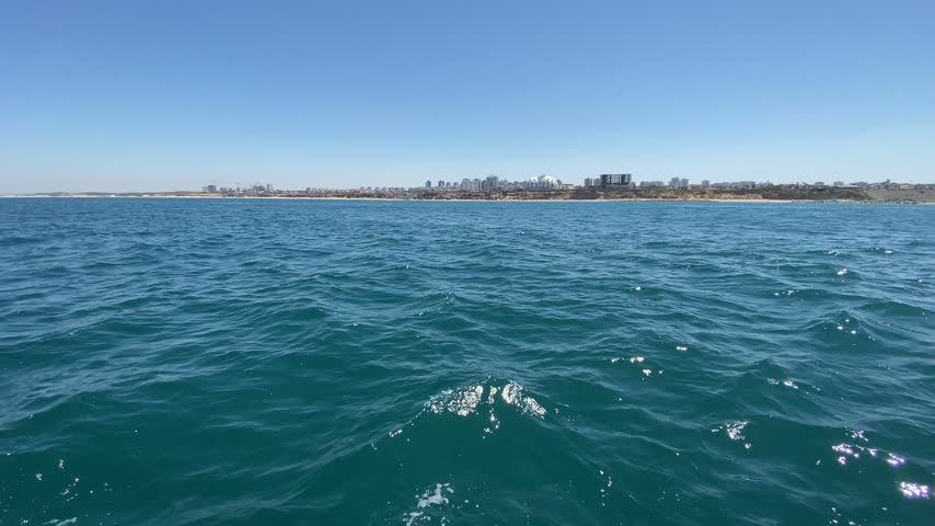 Choppy sea with a distant city coastline seen from a boat, Israel