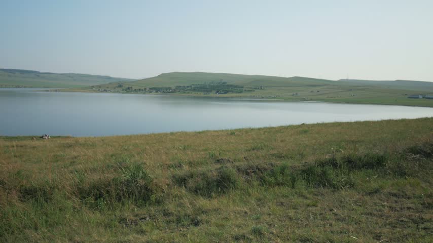 A scenic panoramic landscape of mineral salt Lake Tus surrounded by green steppe hills and rolling grasslands in Khakassia, Russia, during a bright summer day.