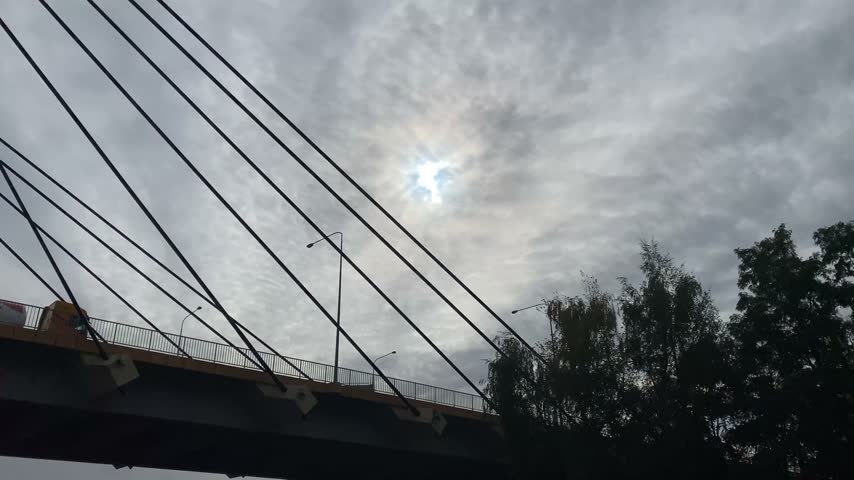 Cable Stayed Bridge Against Cloudy Sky with Sunlight Breaking Through Clouds. Modern Bridge Architecture, Steel Cables and Dramatic Cloudscape.