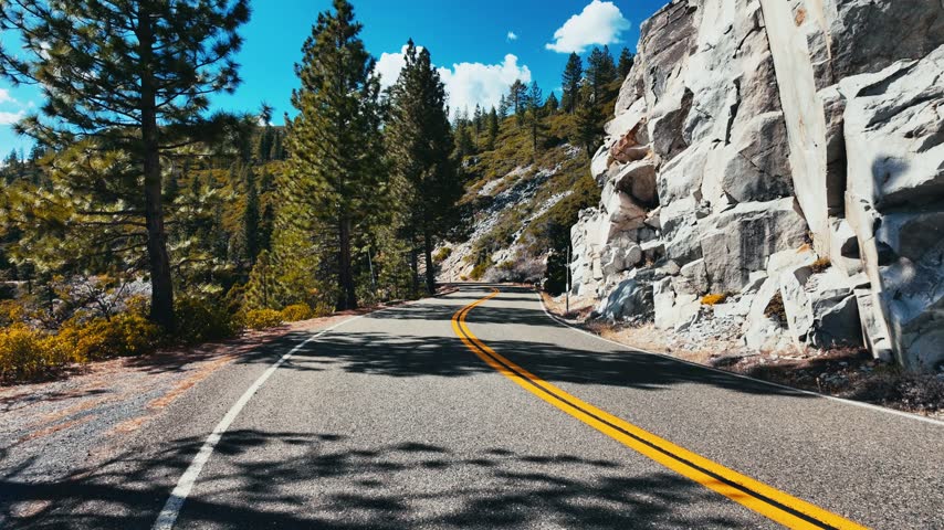 A mountain road winds past steep granite rock faces and pine trees