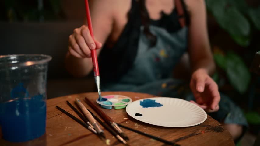 Creative painter preparing acrylic paint with a brush on a paper plate in an art studio