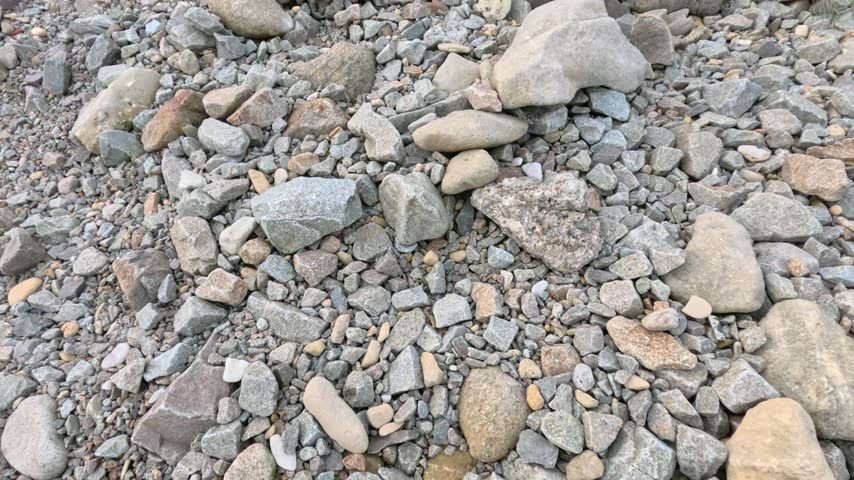 Close up overhead view of diverse river stones and pebbles scattered across natural ground forming rough gravel texture surface.