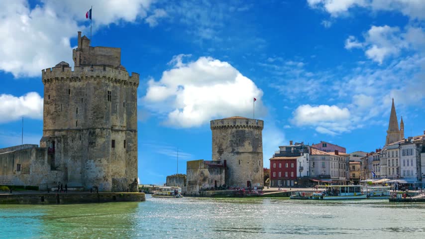 Port of La rochelle guarded by tour de la chaine and tour Saint Nicholas, FranceTime Lapse of the harbor in La Rochelle France. The famous French city on the ocean. Sunny summer day, clouds are moving in the background. Crowds of tourists walk the streetsPort ofrochelle guarded by tour de  chaine and tour Saint Nicholas, FranceLa Rochelle , France Old port, Saint Nicholas and Chain towers