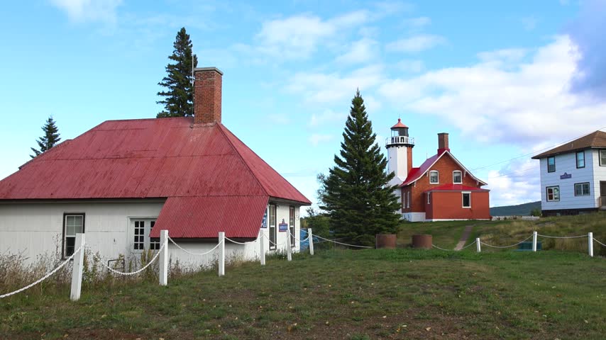 Picturesque red and white lighthouse station on a grassy hill under a partly cloudy sky.