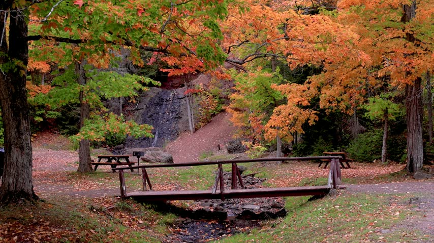 Beautiful park landscape with colorful trees, a creek, a wooden bridge, and a distant waterfall in Michigan upper peninsula .