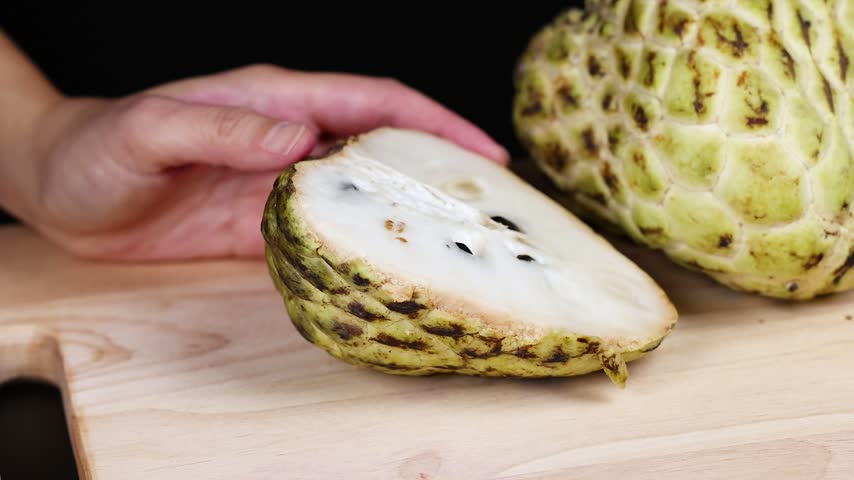 Person cutting ripe cherimoya fruit into quarters with sharp knife, organic healthy food preparation clip.