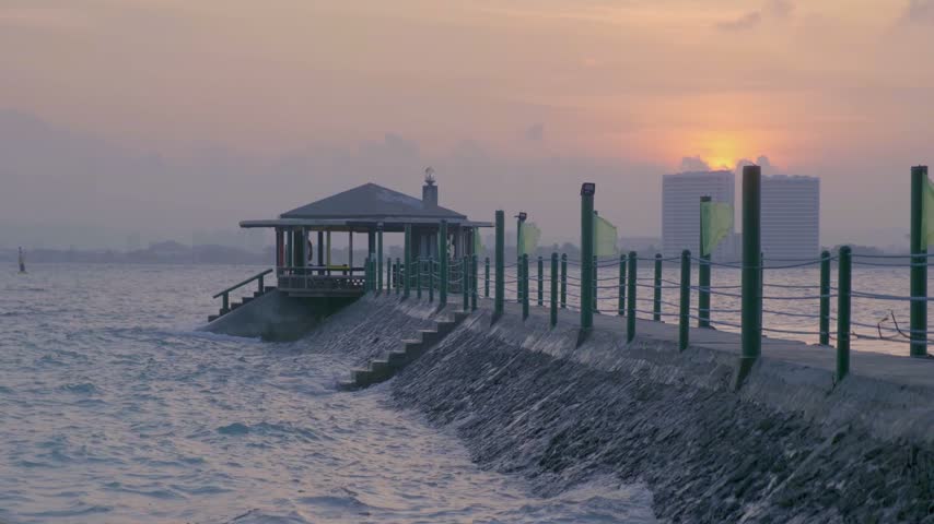 Waves reach a shore pavilion and pier at a tropical resort on Samal Island, Philippines, as the sun sets over the sea.