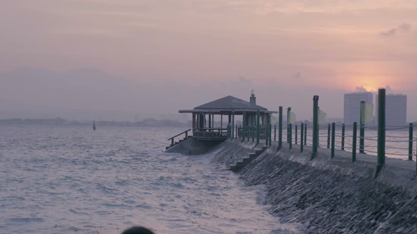 Waves reach a shore pavilion and pier at a tropical resort on Samal Island, Philippines, as the sun sets over the sea.