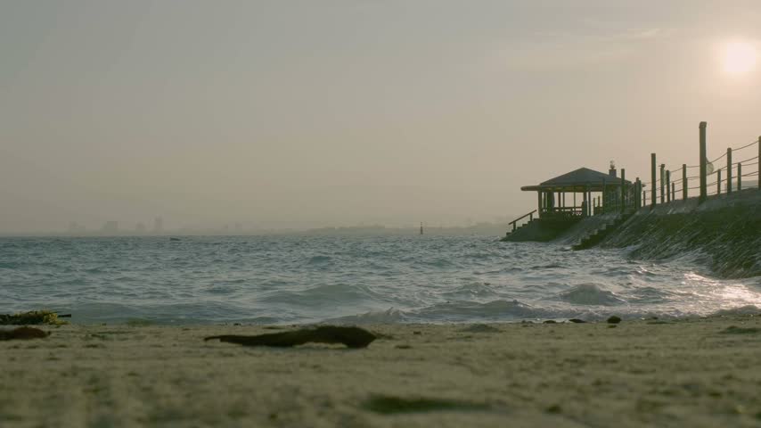 Small waves reach the sandy shore as the sun sits near the horizon beside a fenced walkway at a tropical resort on Samal Island, Philippines.
