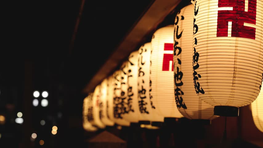 Close up view of illuminated white paper lanterns hanging in row outside traditional japanese shrine at night calm atmosphere.