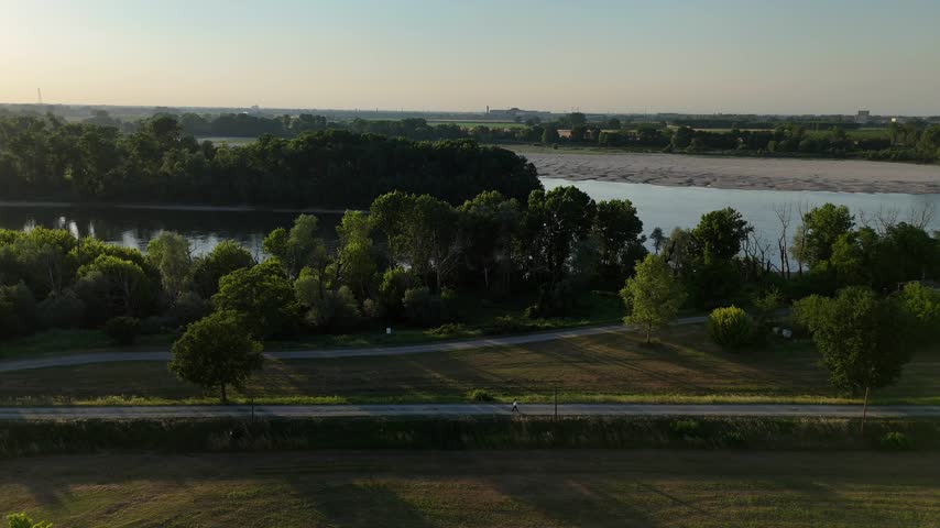 Lanca della Maginot near the Po River with person walking along riverside path, mature trees, grassy embankment, water channel and Po Valley countryside in Monticelli d