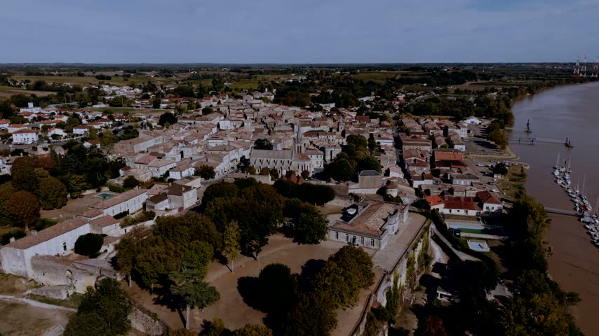 Upper town of Bourg in Gironde, France, with its parish church, the walled citadel park, a marina pontoon on the river and power pylons in the distance.