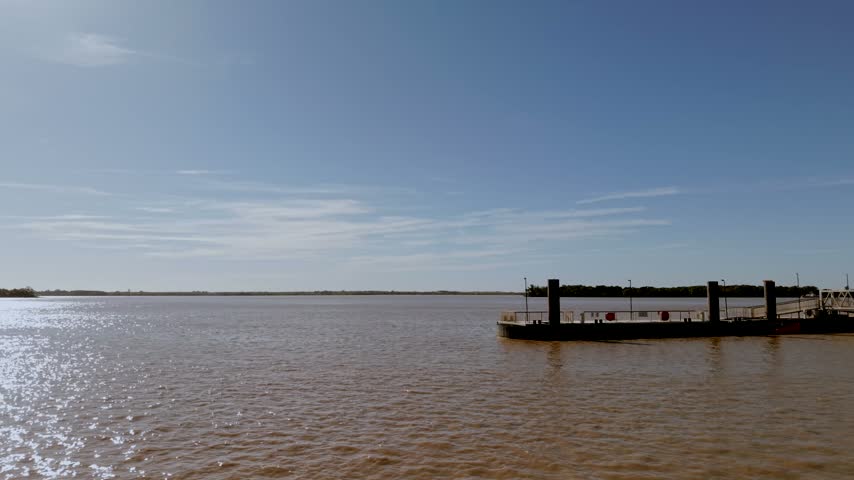 Steel pontoon on the brown water of the Gironde estuary at Blaye, France, a stop for river ferries and cruise boats, with islands low on the horizon.