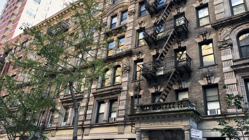 Historic apartment building with fire escapes and trees on a city street in daylight