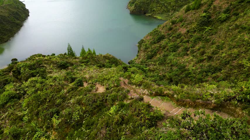 Aerial view of winding hiking trail along lush green hillside above a scenic lake