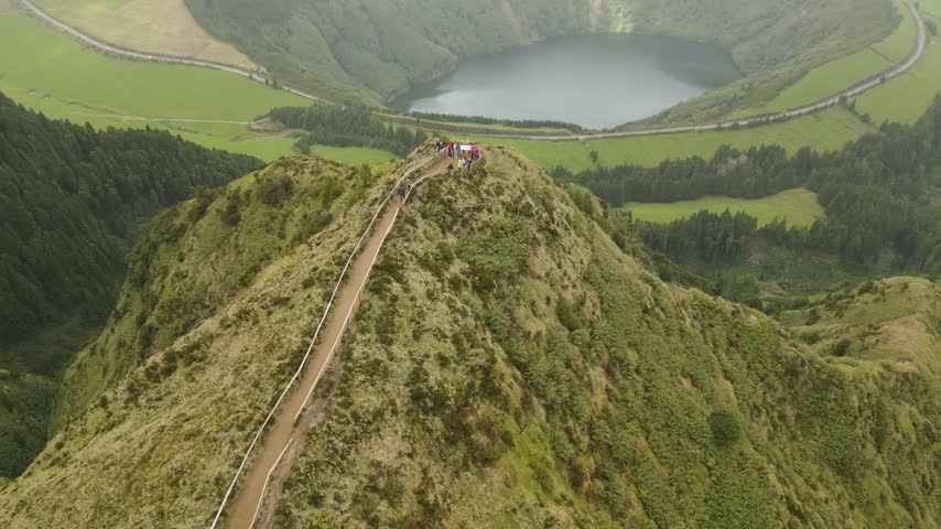 Aerial view of hikers on a scenic mountain ridge overlooking a crater lake below